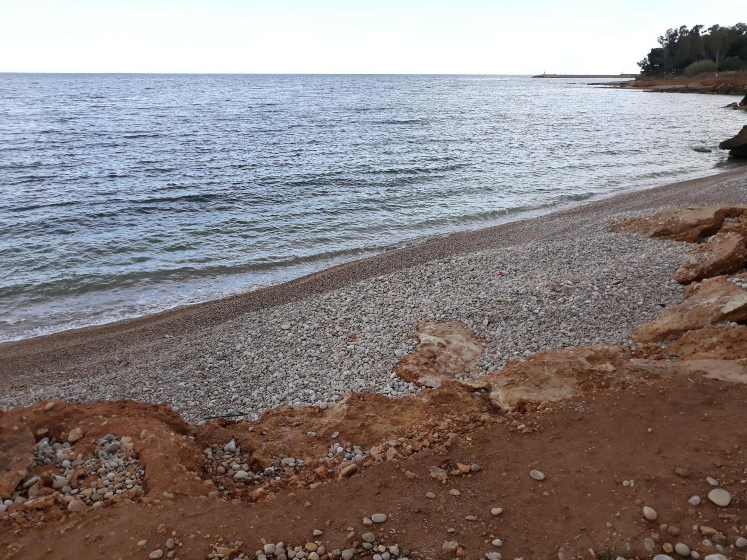 A pebbled beach with a rocky shoreline and calm sea.