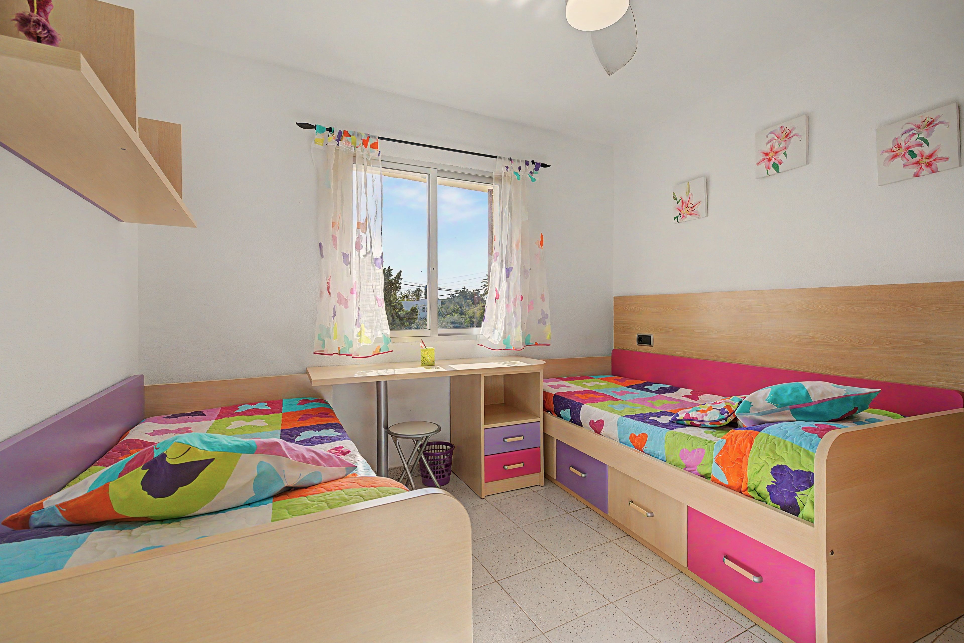 Un dormitorio infantil con dos camas, un escritorio y una ventana con cortinas.