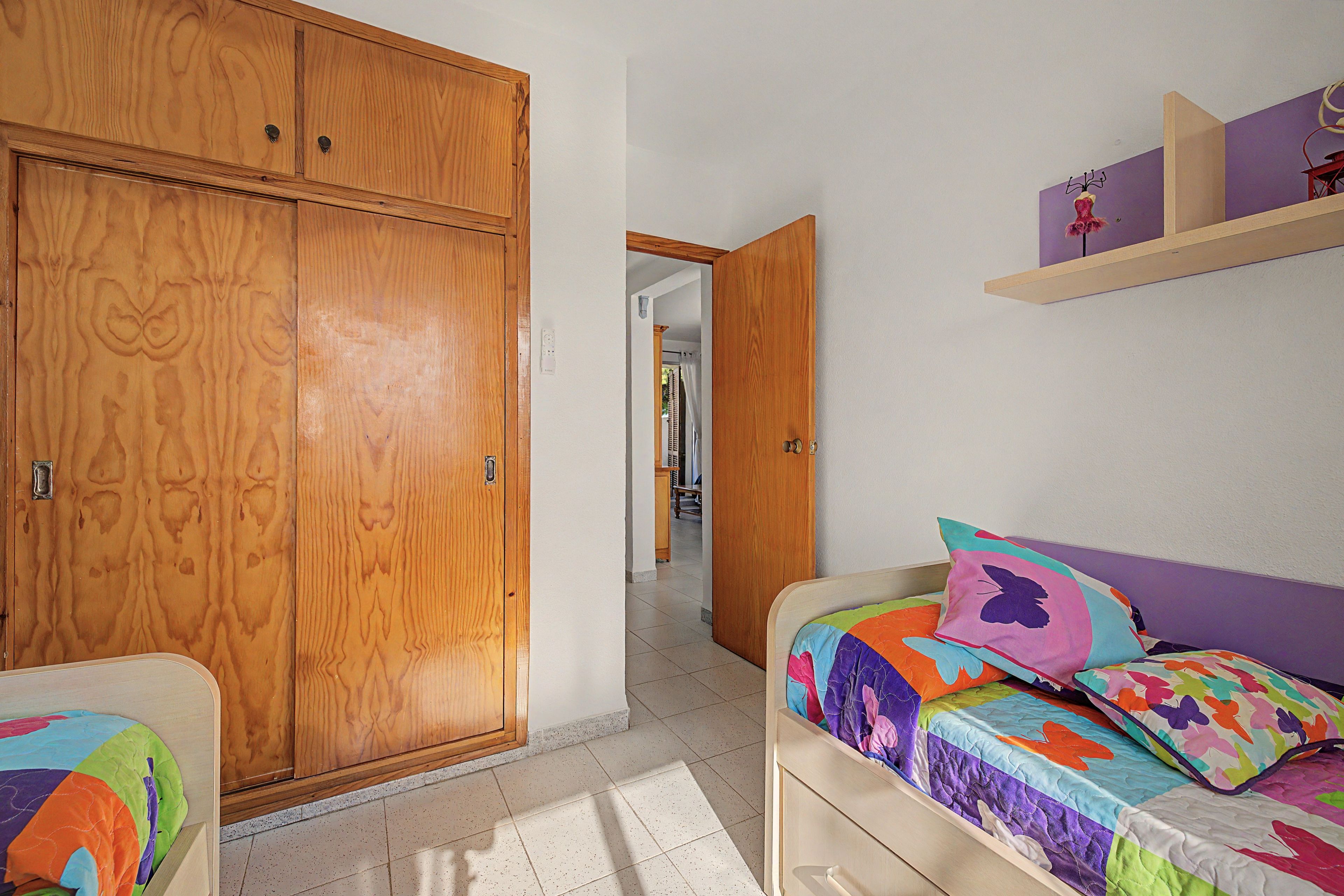 Un dormitorio con un armario de madera, una cama con ropa de cama colorida y una estantería con objetos decorativos.