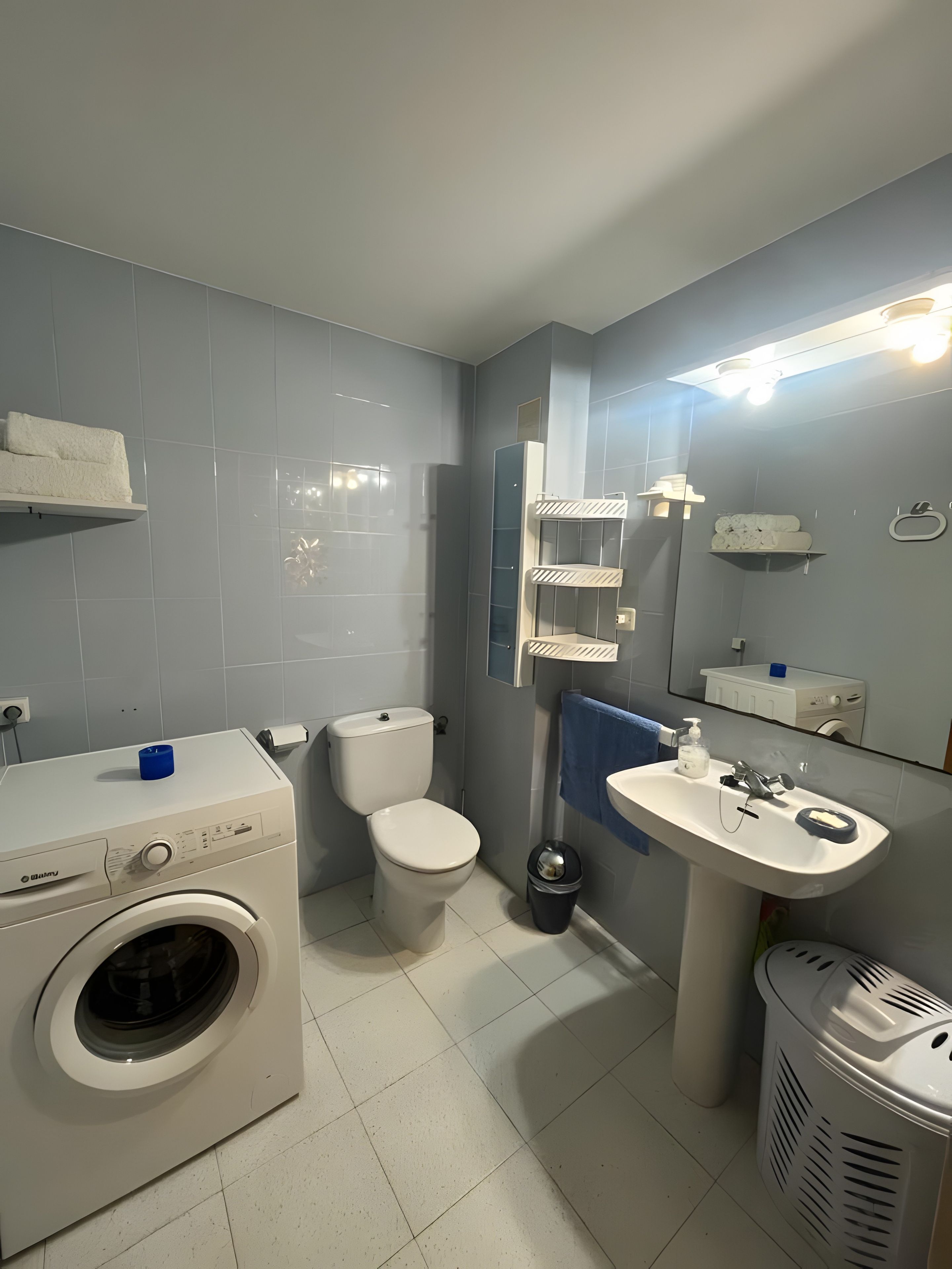 Een moderne badkamer met een wasmachine, toilet, wastafel en een spiegel met verlichting.