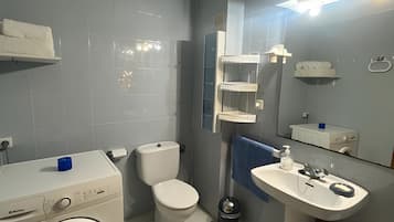 Een moderne badkamer met een wasmachine, toilet, wastafel en een spiegel met verlichting.