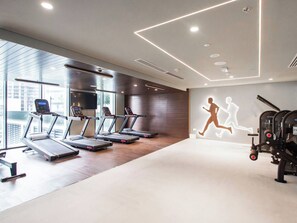 A modern gym with treadmills, a wall projection of a running figure, and large windows. - Chic 1BR Escape in Creek Edge | Creek Harbour (Dubai)