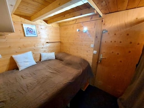 A small, cozy room with wooden walls and a sloped ceiling. There is a single bed with two pillows and a small table with a lamp. - Arc 2000 Splendide 5* (Renovated) Ski-In/Ski-Out, Wi-Fi (Bourg-Saint-Maurice)