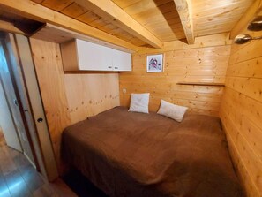 Ein kleiner Holzraum mit einem Bett, einem weißen Schrank und einem gerahmten Bild an der Wand.