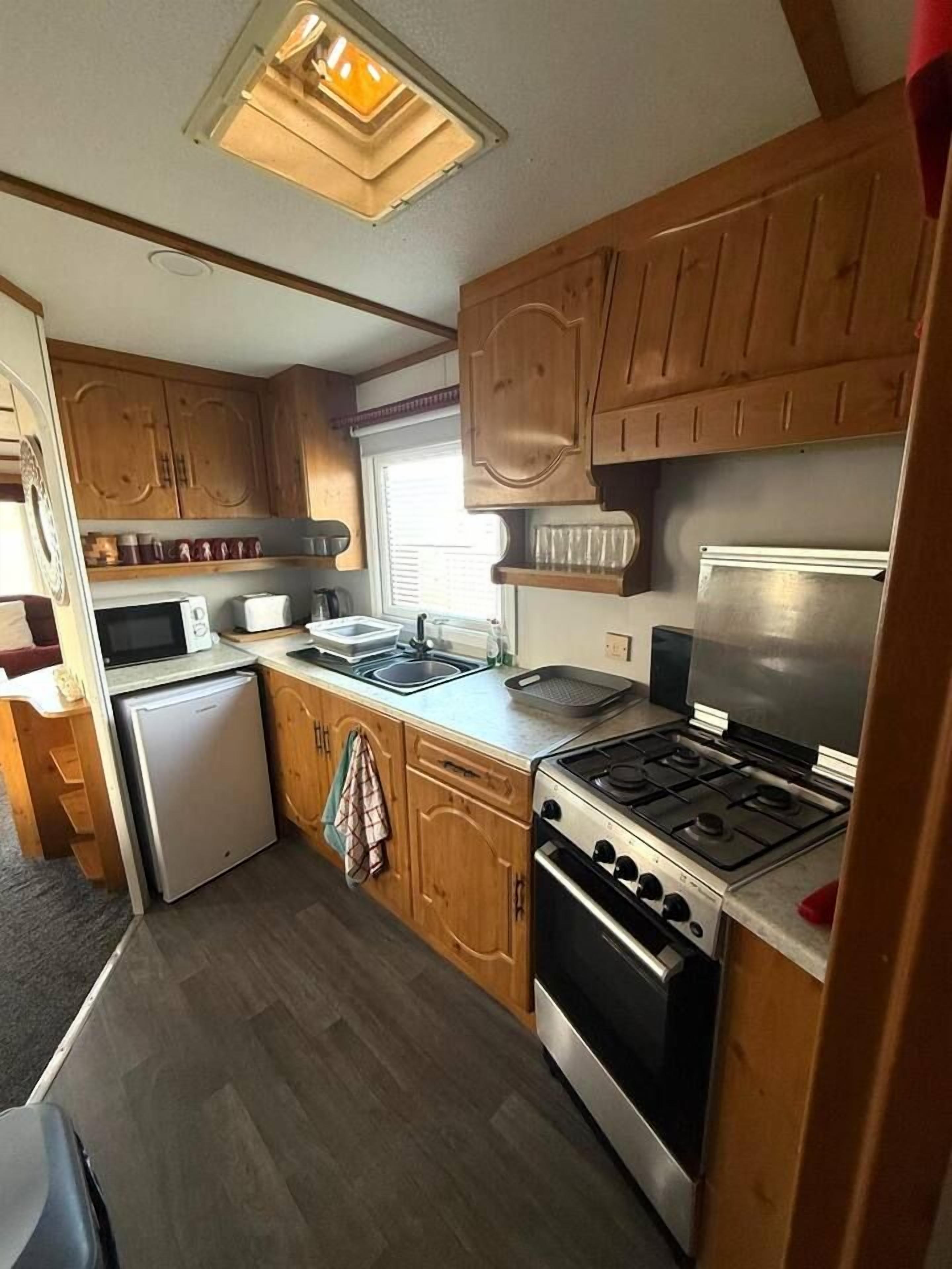 Une cuisine compacte avec des meubles en bois, un réfrigérateur, un four à micro-ondes, une cuisinière et un évier.