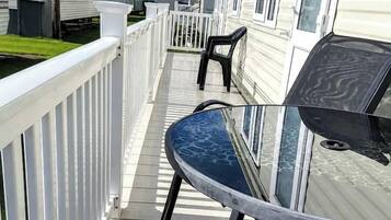 A deck with a table and chairs, surrounded by a white railing, with mobile homes in the background.