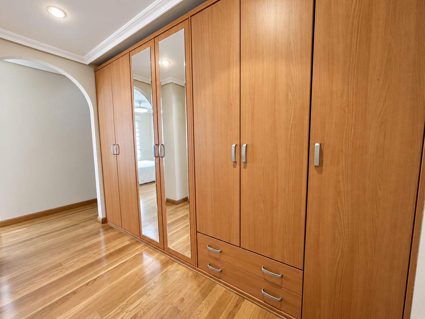 Una habitación amplia con un gran armario de madera, un espejo y piso de madera.