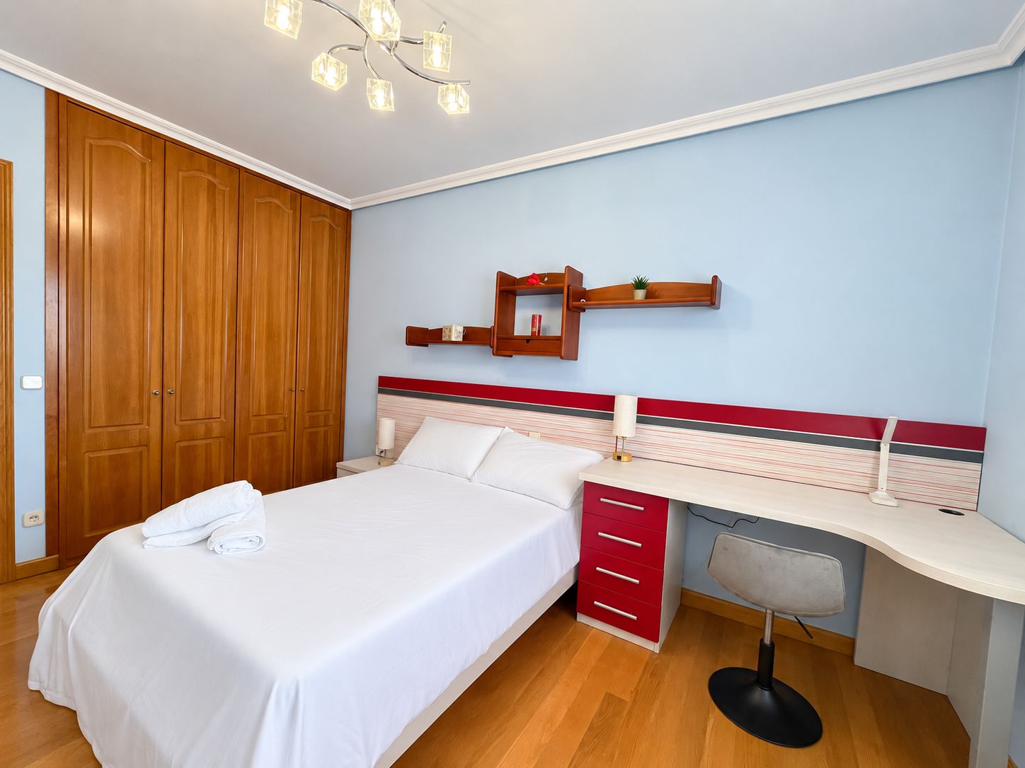 Habitación de hotel con cama, escritorio, silla, armario y estante en la pared.