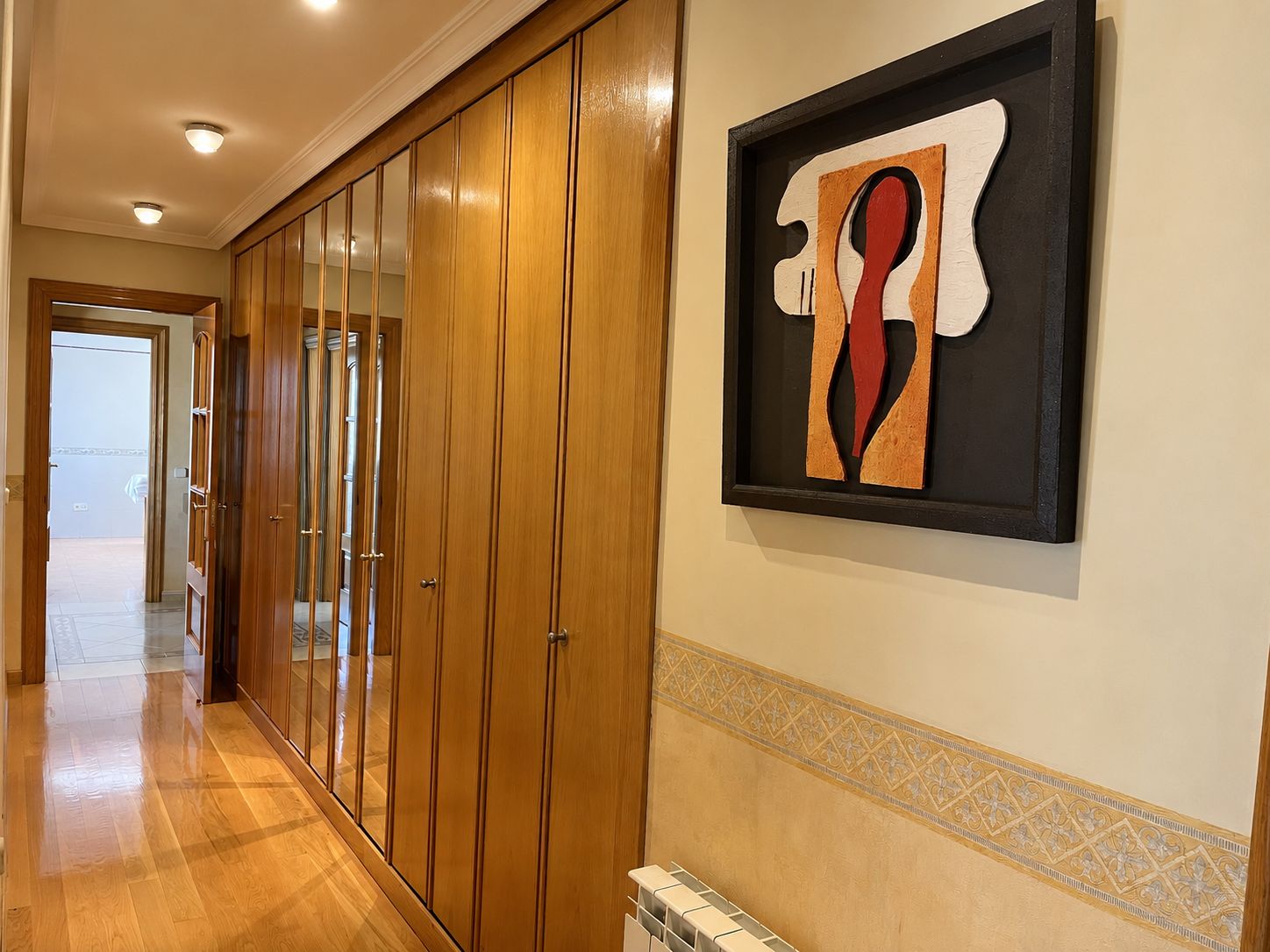 A hallway with wooden doors and a framed abstract artwork on the wall.