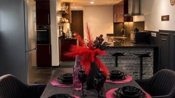 Een moderne eethoek met een zwarte tafel voor vier personen, een decoratieve rode veerraamstelling, en een keuken op de achtergrond.
