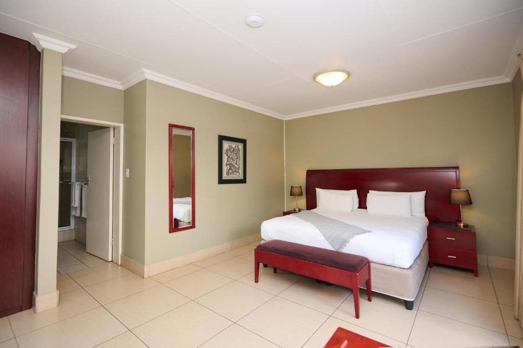 Una habitación de hotel con una cama grande, una mesita de noche, un banco, un espejo y una puerta que da a un baño.