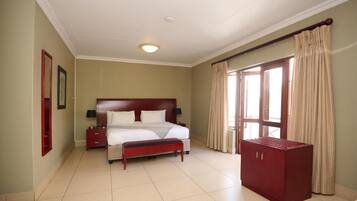 Una habitación de hotel con una cama grande, una mesita de noche, un banco, un armario y una ventana con cortinas.