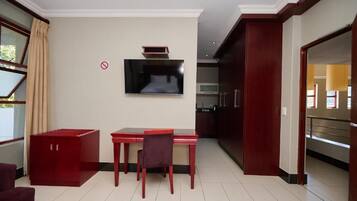 Habitación de hotel moderna con zona de comedor, televisor de pantalla plana en la pared y vistas al exterior a través de una ventana.