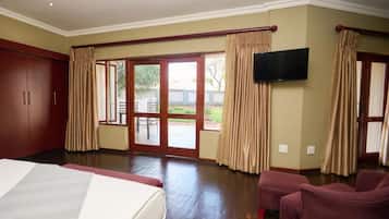 A hotel room with a large bed, a flat-screen TV mounted on the wall, and a sliding glass door leading to an outdoor area.