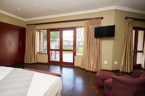 Habitación de hotel con una cama grande, un televisor de pantalla plana montado en la pared y una puerta corrediza de vidrio que da a un espacio exterior.