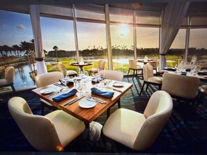 A dining area with tables set for four, large windows with a view of a body of water and greenery, and a carpeted floor. - DIVI VILLAGE GOLF & BEACH RESORT - 1 BEDROOM SLEEPS 4. STEPS AWAY FROM THE BEACH (Oranjestad)