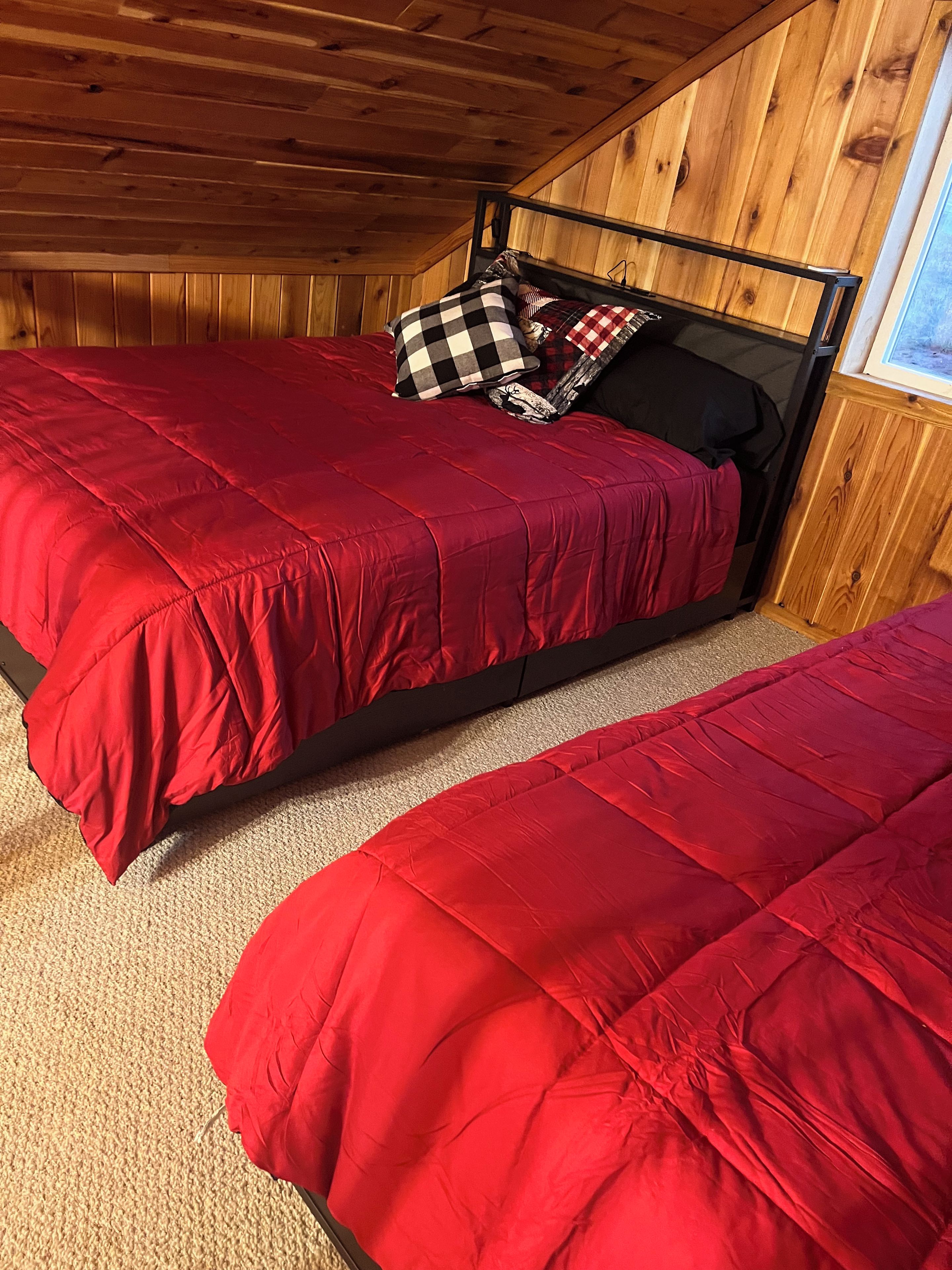 A bedroom with a sloped ceiling, a bed with a red bedspread, and a checkered pillow.