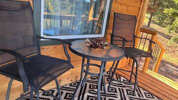 Terraza de madera con puerta de vidrio, dos sillas, una mesa y un tapete estampado.