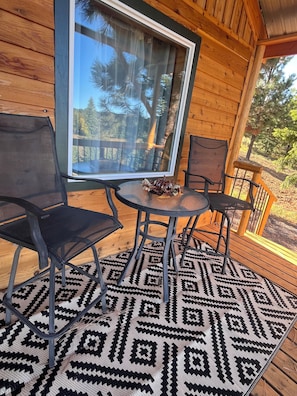Eine Holzterrasse mit Glastür, zwei Stühlen, einem Tisch und einem gemusterten Teppich.