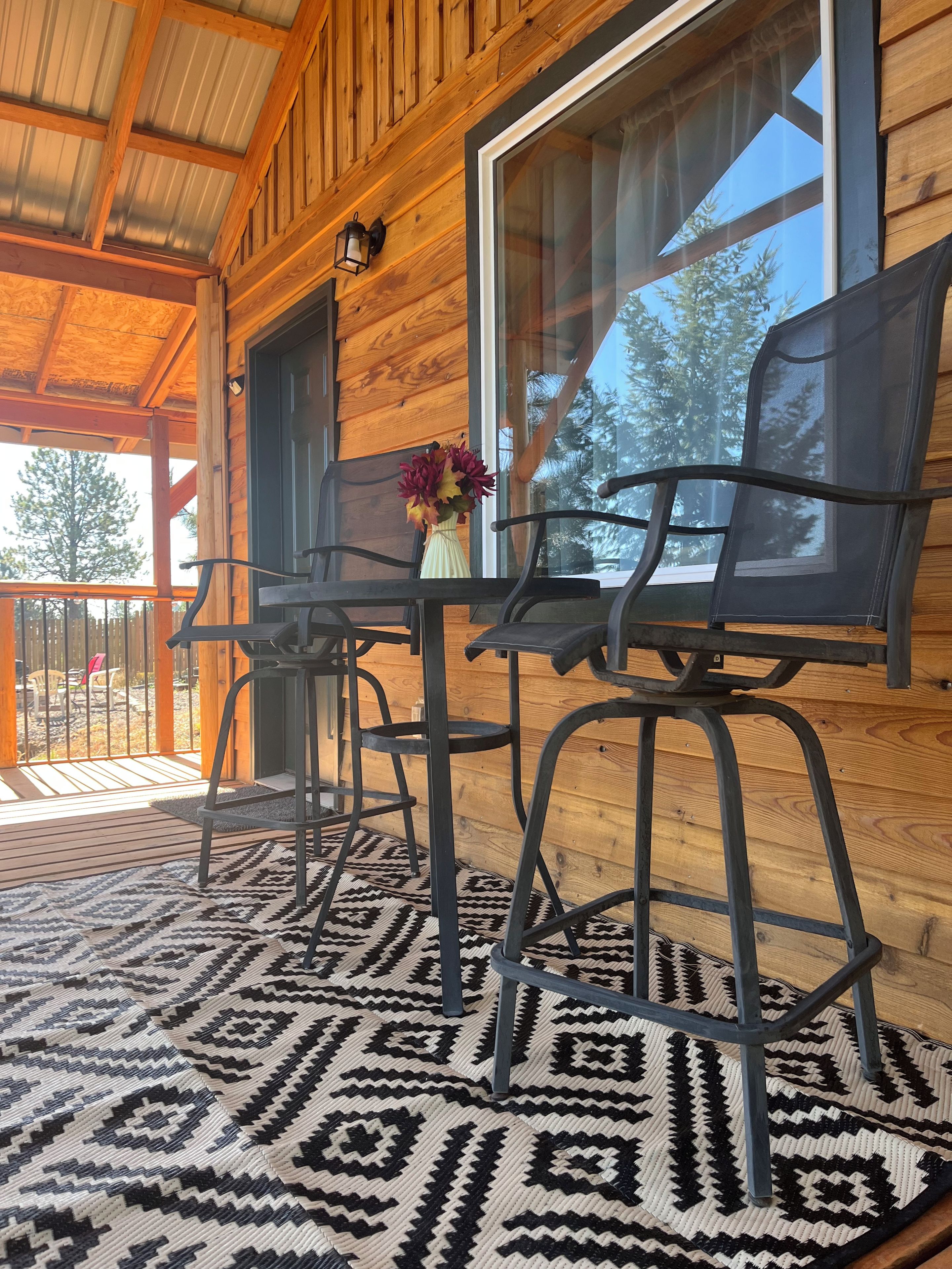 A wooden cabin with a covered porch, a dining table with chairs, and a large window.