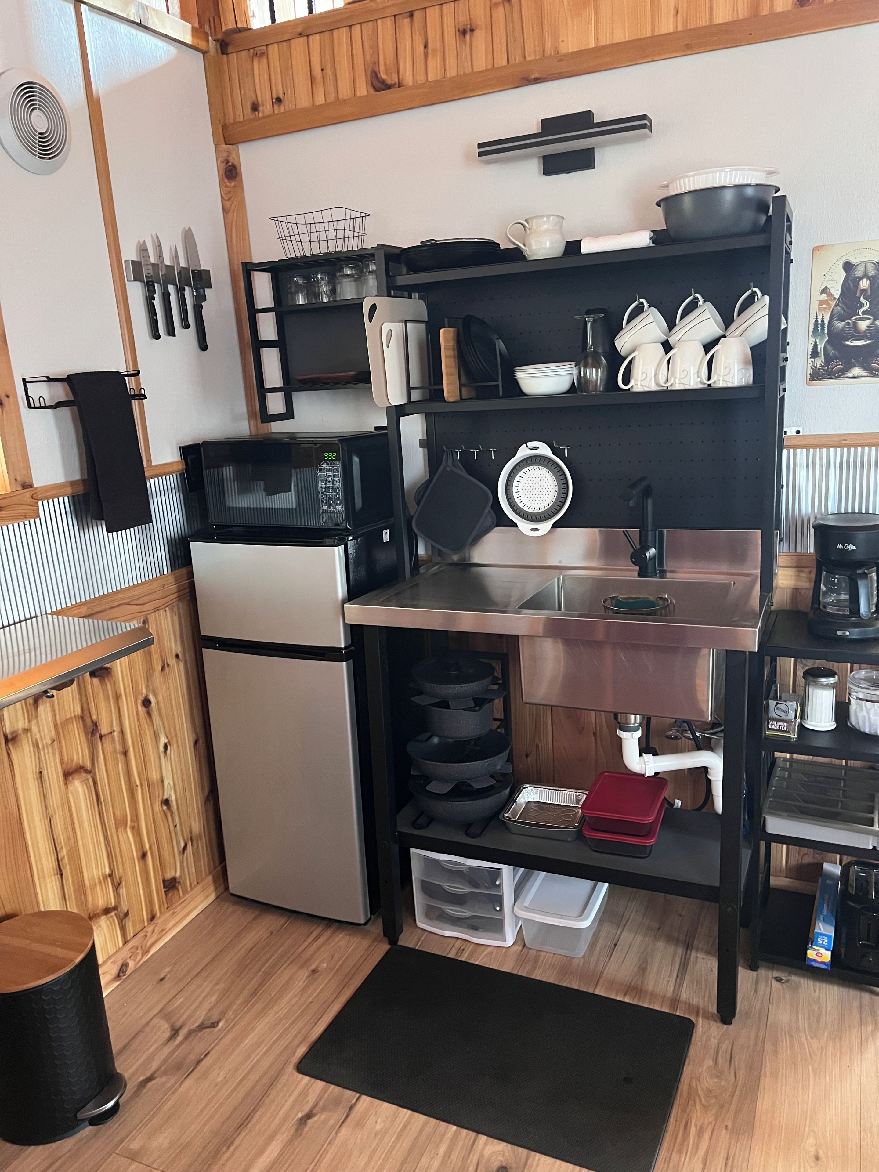 A compact kitchen with a microwave, stove, and sink. There are utensils hanging on the wall, and a coffee machine on the counter.