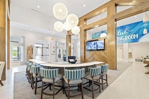 A modern bar area with a curved counter and bar stools, a television screen, and a 'Club Room' sign. - Landing Spectacular 1BD in Clara Avenue (Panama City Beach)