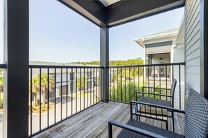 Un espace extérieur abrité doté d’une terrasse en bois, d’une rambarde en métal et d’un coin salon avec une chaise et un canapé.