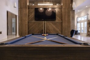Une table de billard avec un cadre en bois, un téléviseur fixé au mur et un drap de jeu bleu.