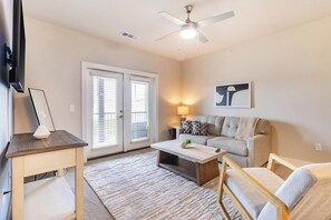 Un salon comprenant un canapé, une table basse, un téléviseur, un ventilateur de plafond et une porte avec des stores.