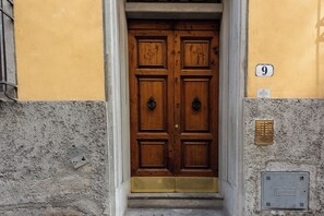 A wooden double door with a brass knock plate, a number plaque, and a metal intercom on a textured wall. - Borgo Tegolaio House by MMega (Firenze)