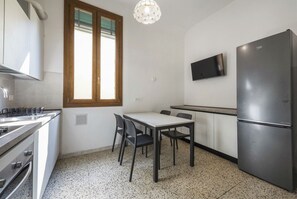 A compact kitchen with a dining table and chairs, a built-in oven, a refrigerator, and a TV mounted on the wall. - Borgo Tegolaio House by MMega (Firenze)