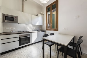 A modern kitchen with a microwave, stove, oven, and a dining area with a table and chairs. - Borgo Tegolaio House by MMega (Firenze)