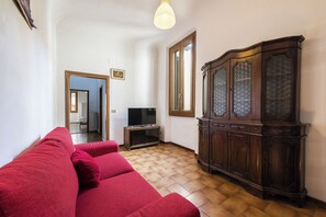 Un salon avec un canapé rouge, un téléviseur posé sur un meuble et un buffet en bois.