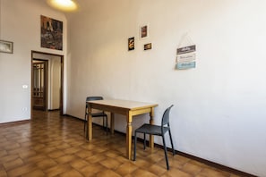 Une pièce avec une table en bois et deux chaises, une porte donnant sur une autre pièce, et un mur orné d’une affiche et de quelques panneaux d’encouragement.