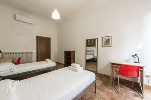 A hotel room with two single beds, a desk with a chair, a radiator, and a mirror. - Borgo Tegolaio House by MMega (Firenze)