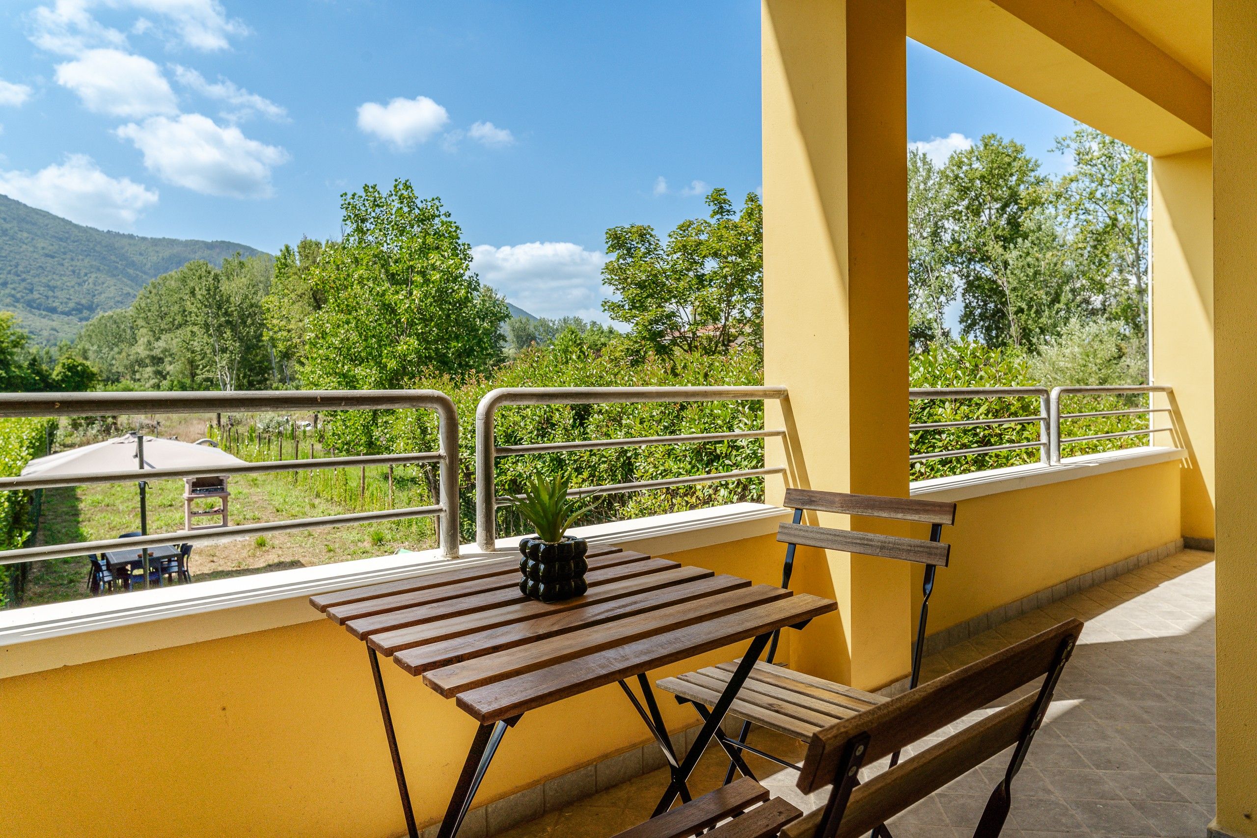 Ein Balkon mit Holztisch und -bank, einem Blumentopf und Blick auf eine Berglandschaft.