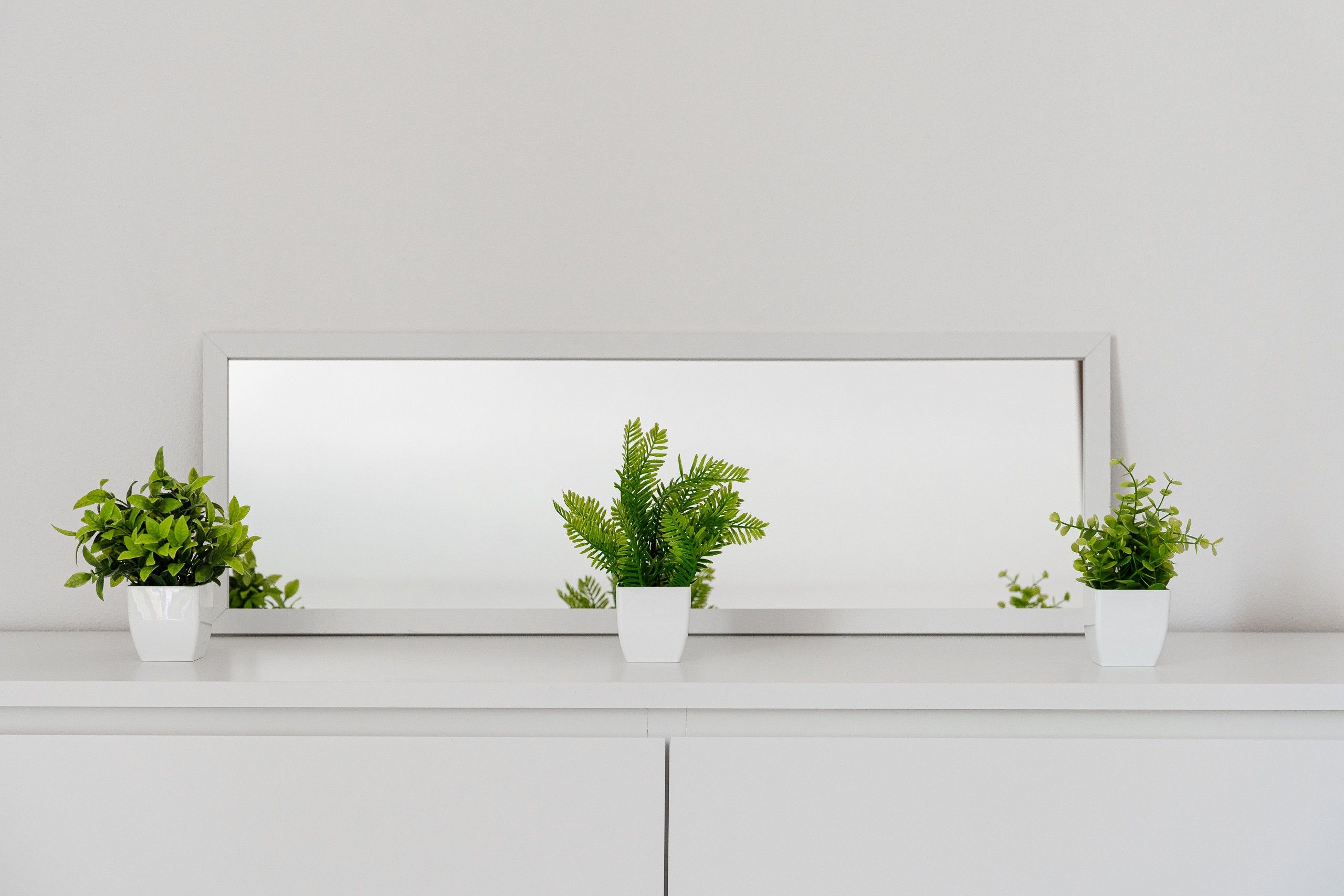 Une étagère blanche sur laquelle sont posées trois pots blancs contenant des plantes vertes.