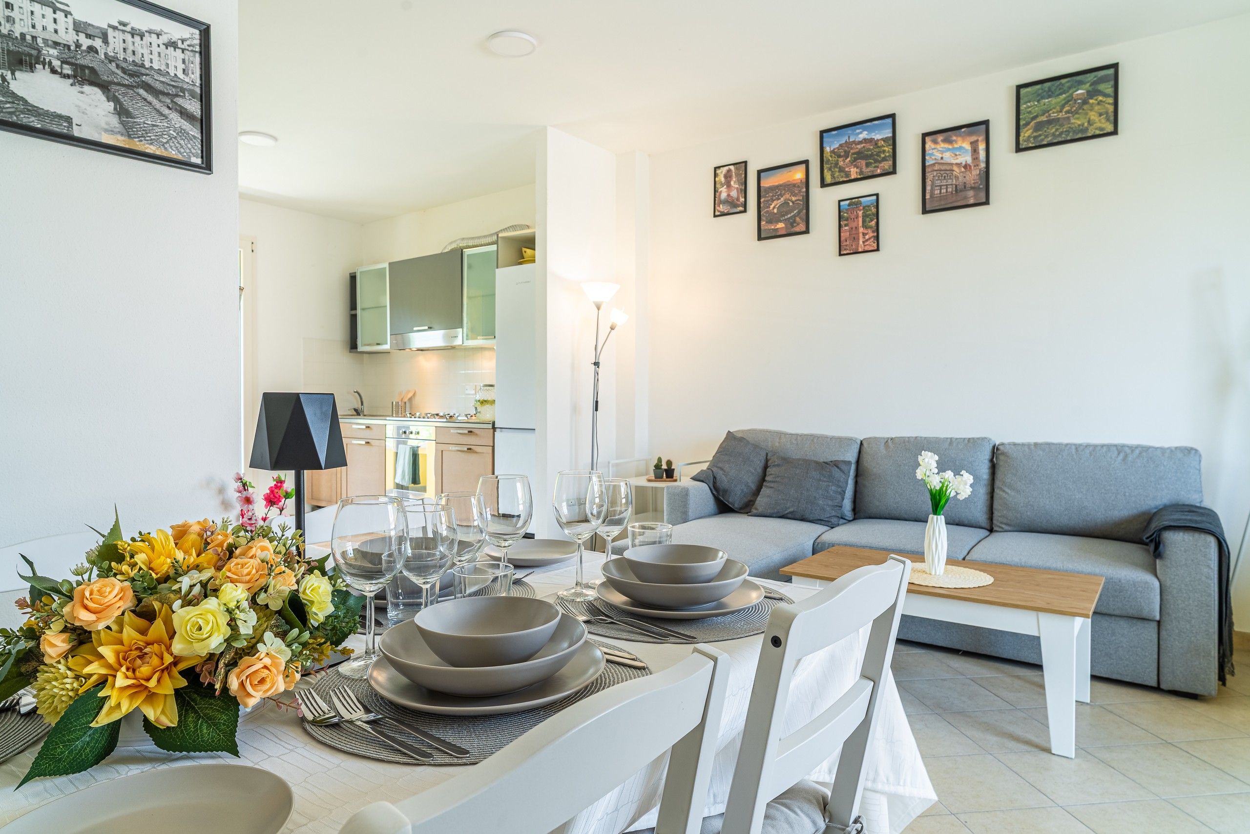 Ein modernes Wohnzimmer mit Essbereich, grauem Sofa und einer Küche im Hintergrund.
