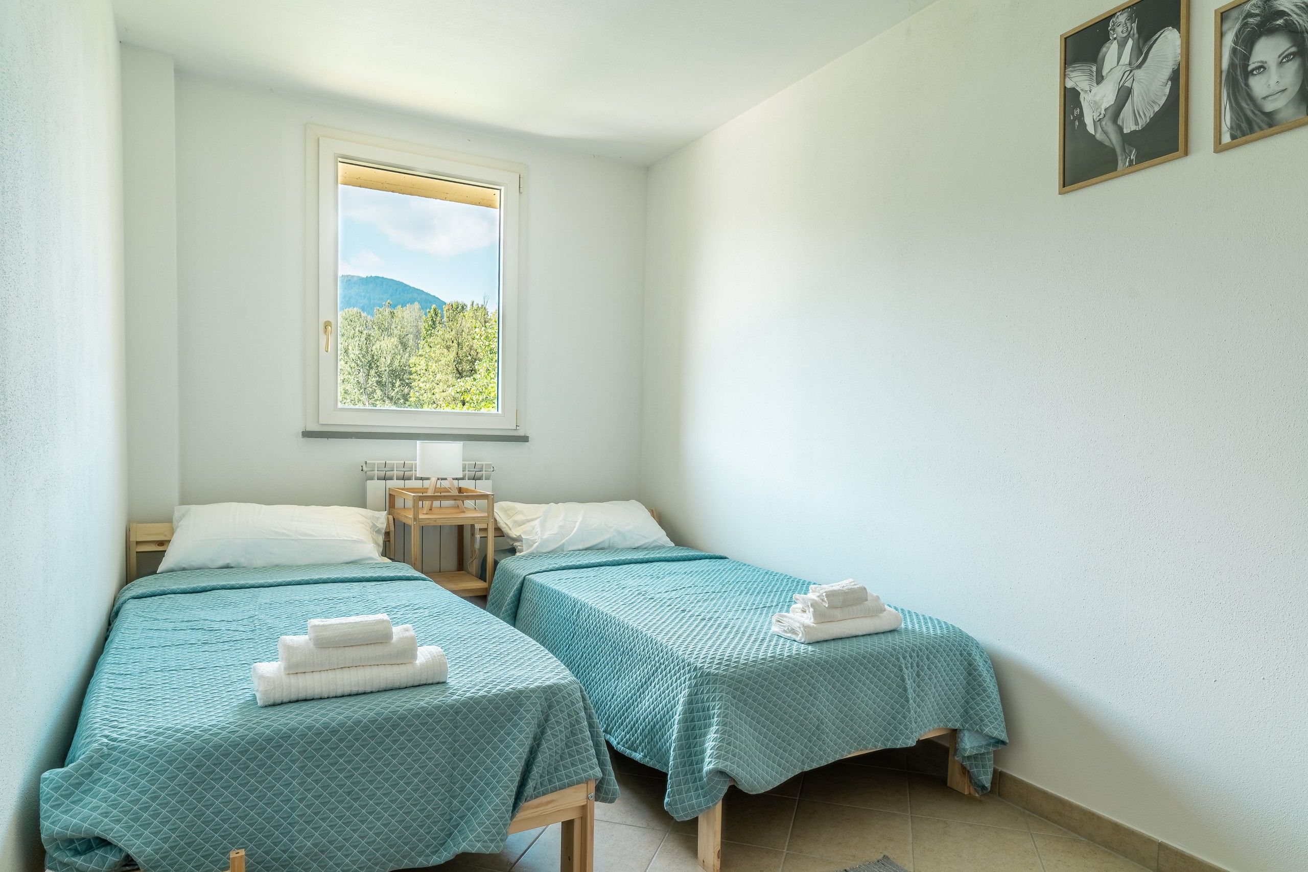 A small, clean room with two beds, a window with a mountain view, and a wooden chair.