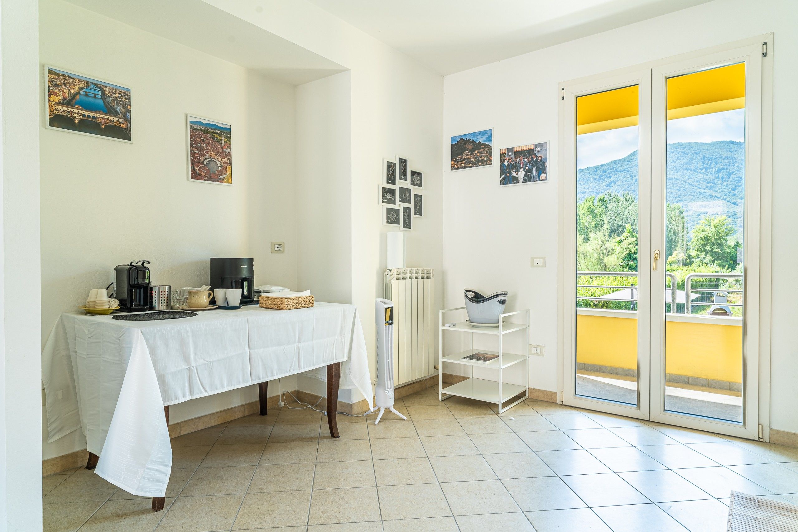 Una stanza con un tavolo apparecchiato per la colazione, un termosifone e vista sul verde attraverso una porta scorrevole.