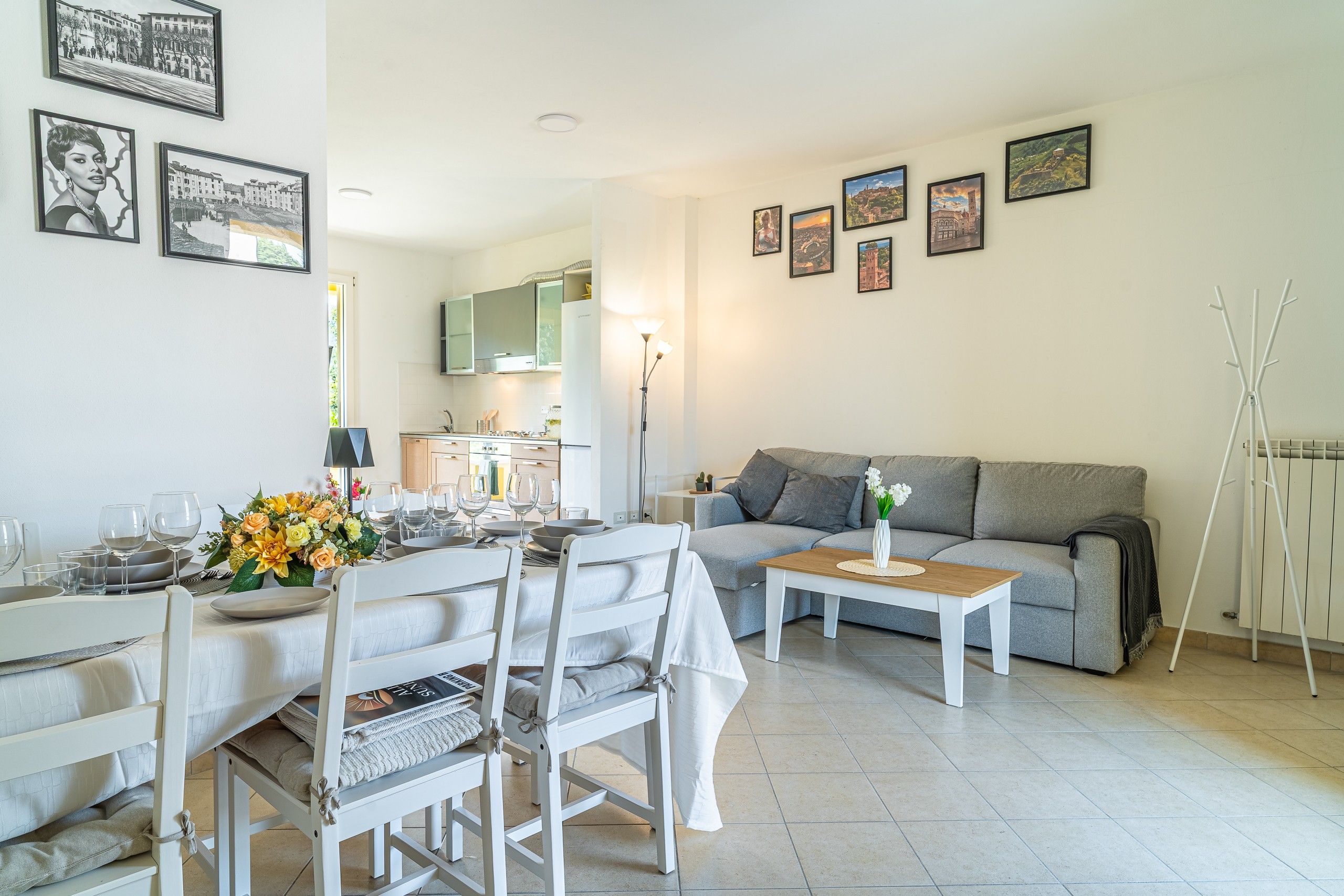 Un soggiorno moderno con zona pranzo, un divano grigio e un tavolino da caffè. Alle pareti ci sono quadri incorniciati e un termosifone a pavimento.