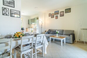 Un salon moderne avec un coin repas, un canapé gris et une table basse. Des tableaux encadrés ornent le mur et un radiateur est posé sur le sol.