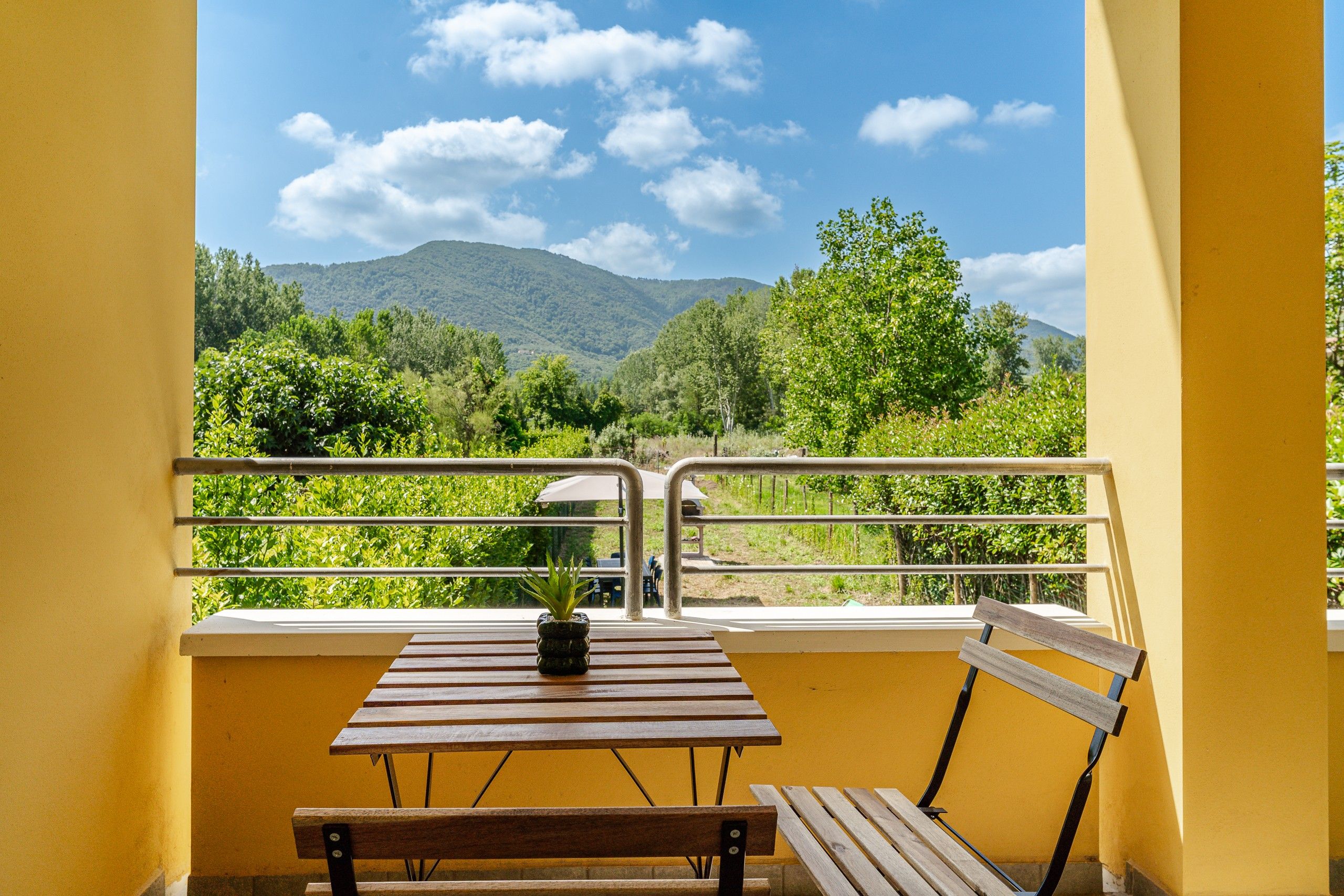 Ein Balkon mit Holztisch und Bank, der Blick auf Berge und Grünflächen bietet.