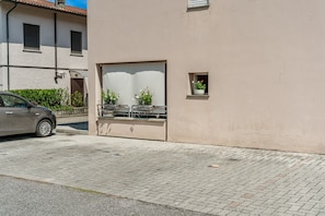 A building with a paved entrance, a car parked outside, and a small window with a potted plant.