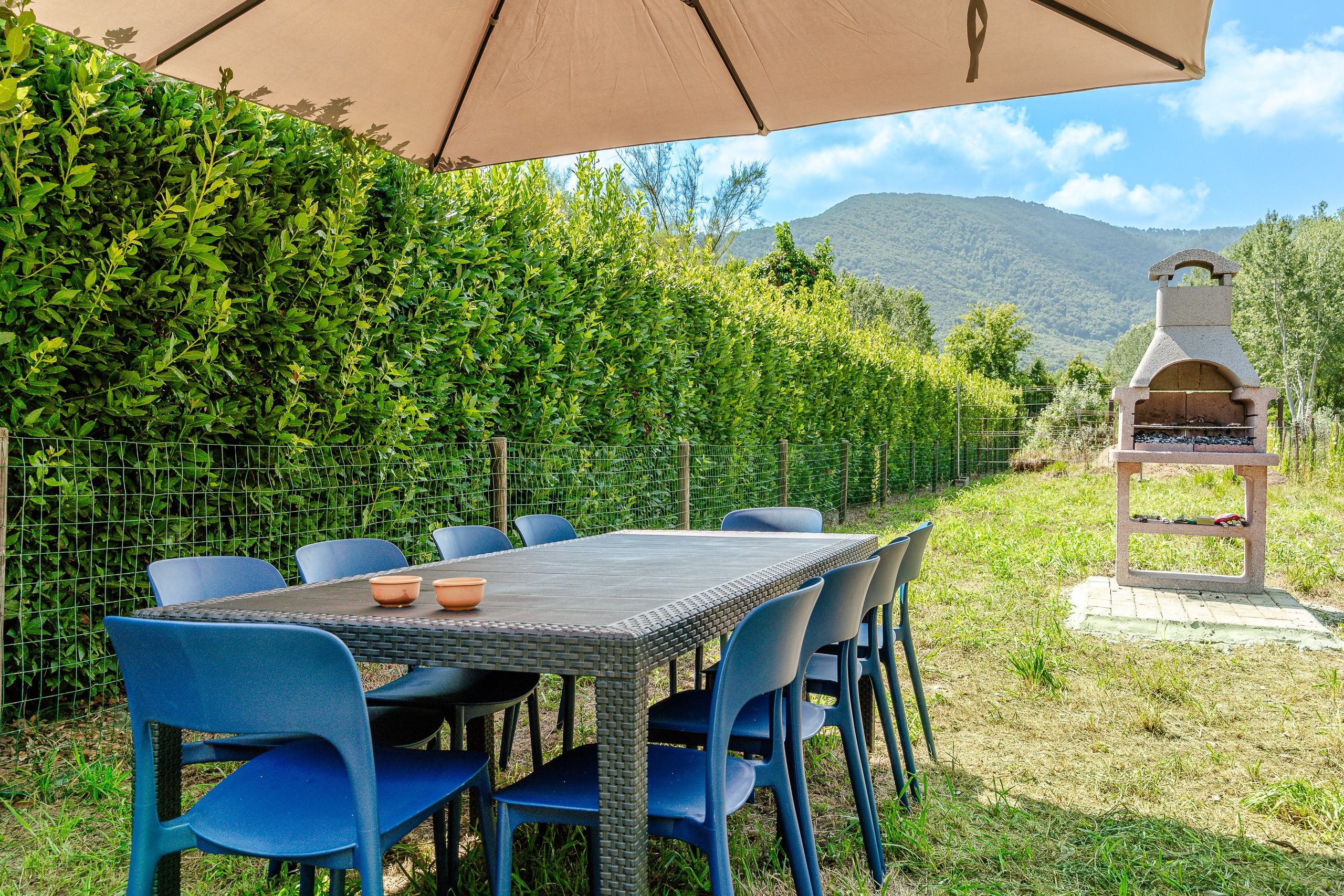 An outdoor dining area with a table and chairs, a barbecue grill, and a view of a mountain.