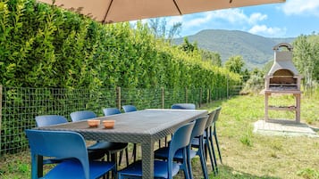 An outdoor dining area with a table and chairs, a barbecue grill, and a view of a mountain.