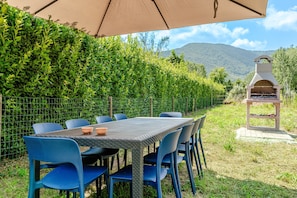 An outdoor dining area with a table and chairs, a barbecue grill, and a view of a mountain. - Holiday Home 'Alba Sunrise - Ac Hot Tub Parking' with Wi-Fi and Air Conditioning (Lucca)