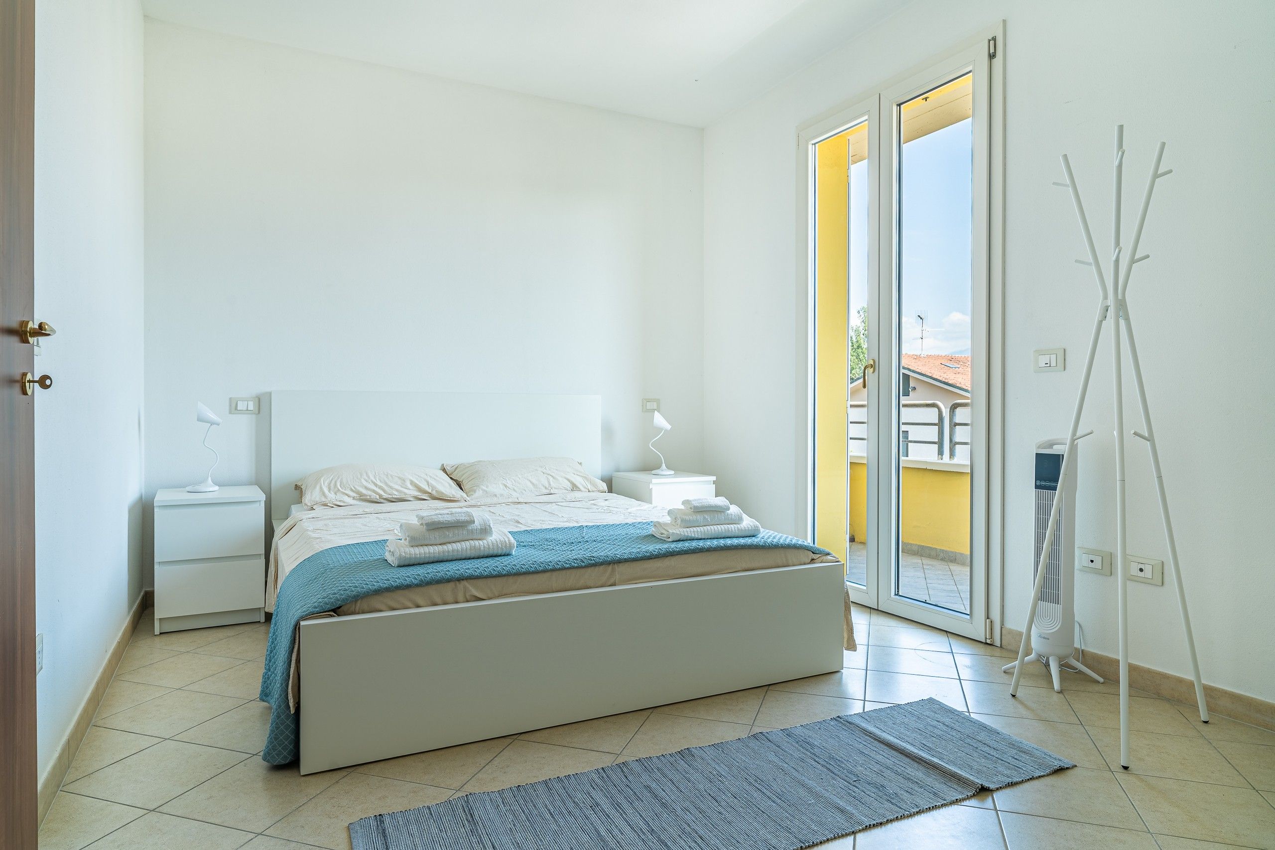 Ein Schlafzimmer mit Bett, Nachttischen, einer Lampe, einem Fenster und Blick ins Freie.