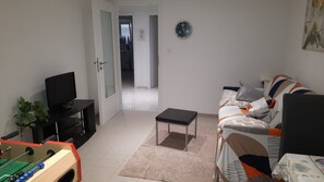 Una sala de estar con un sofá, televisión, una mesita y una mesa de futbolín.