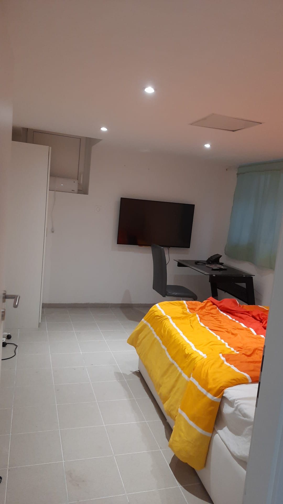 Una habitación de hotel con una cama, un escritorio, una silla, un televisor y una puerta.